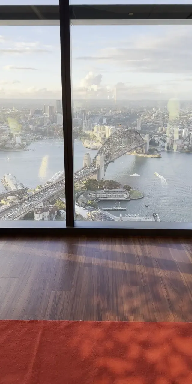 A Bondi Booths 360 booth set up on a red carpet beside floor-to-ceiling windows overlooking Sydney Harbour and the Opera House.